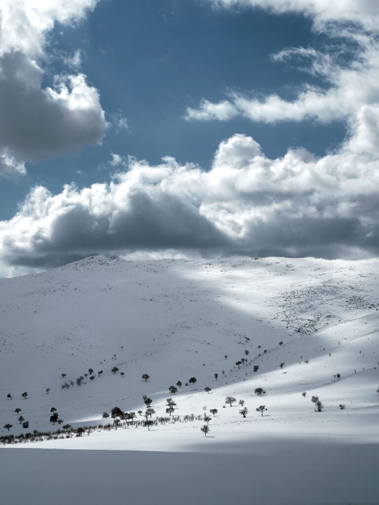 A snowy mountain on a sunny day with low hanging clouds over it.