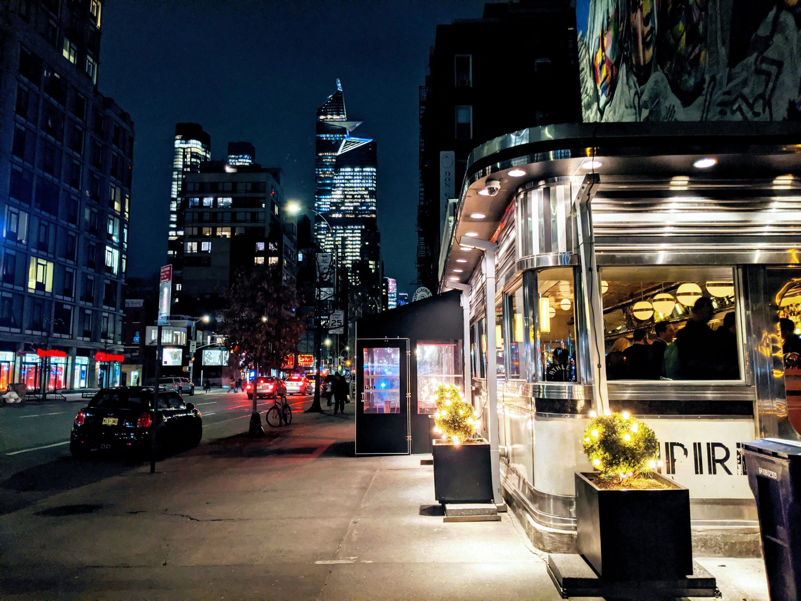 Lit up diner at night in London. Cars on the street, high rises in the background.