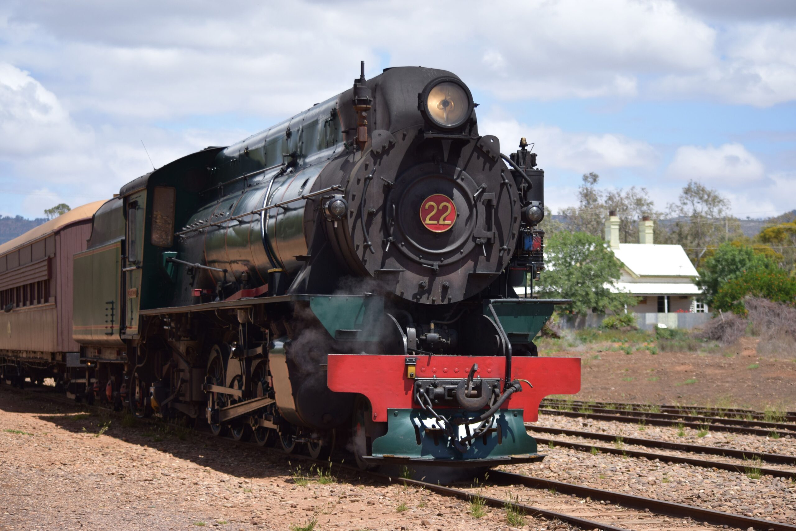 A black train sits on a track with a white building behind it, set against a blue sky.