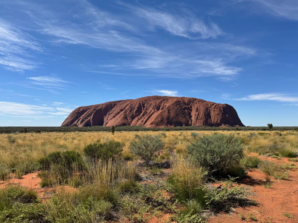 Uluru in Australia surrounded by a blue sky and brush.