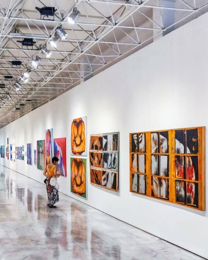 A woman stands in a white room looking at an art exhibit.